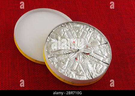 Rad von einzeln geschnittenen Mini-Scheiben Brie Käse in Karton auf roter Tischdecke Stockfoto