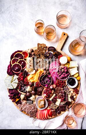 Auswahl an Schokolade, Obst und Käse auf einer Platte neben Gläsern Roséwein. Stockfoto