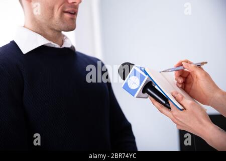 Journalistin Schreiben auf Tagebuch während der Einnahme von einem Interview von Geschäftsmann Stockfoto