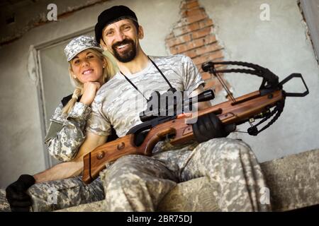 Lächelnde männliche und weibliche Militärs mit Armbrustwaffe sitzen und schauen auf die Kamera. Stockfoto