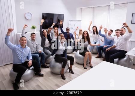 Gruppe von Glücklich erfolgreiche Multi-ethnischen Geschäftsleute sitzen auf Fitness Ball schwenkten ihre Hände in Office Stockfoto