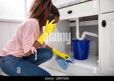 Nahaufnahme einer jungen Frau die blauen Eimer unter Wasser leckt von der Spüle Leitung Stockfoto