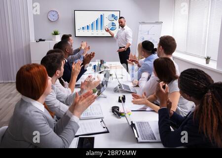 Gruppe von multi-ethnische Leute klatschen für einen erfolgreichen Geschäftsmann, die Darstellung auf dem Bildschirm Stockfoto