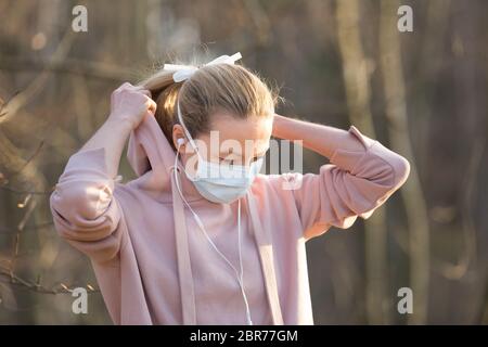 Portrait der kaukasischen Sportfrau, die eine Gesichtsmaske mit medizinischem Schutz trägt, während sie im Park spazieren geht, sich entspannt und Musik hört. Corona-Virus oder Covid Stockfoto