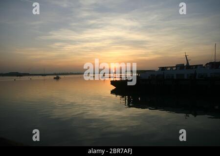 Sonnenuntergang über dem Fluss Crouch in Burnham auf Crouch in Essex. Im Vordergrund liegen die Boote an einem Kai mit anderen Booten auf dem Fluss. Der Stockfoto