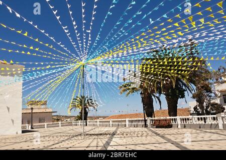 Eine Kirche Platz geschmückt mit bunten Girlanden für ein traditionelles Fest auf Teneriffa. Die blau-weiß-gelben Fahnen wehen im Wind unter einem dunklen Blu Stockfoto