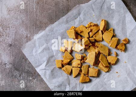 Hausgemachte Honigwaben-Hokey-Pokey oder Schlacktoffee oder Dalgona koreanische Zuckerwaren auf Backpapier auf grauem Betongrund. Flach, Platz Stockfoto