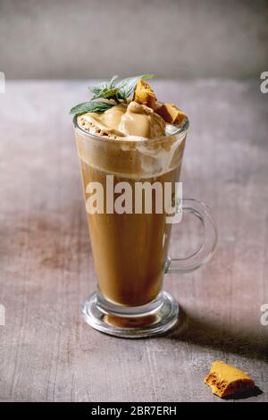 Dalgona schaumig Kaffee Trend koreanisch Getränk Latte Espresso mit Kaffee Schaum in hohen Glas, dekoriert von Dalgona Zinken Toffee Süßigkeiten und Minze. Grau konkar Stockfoto