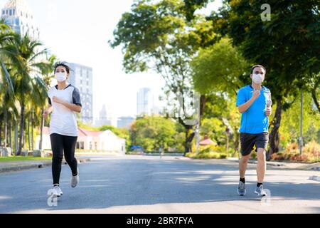 Asiatische junge Paar Frau und Mann sind Joggen und exciseing im Freien in Stadtpark und tragen Schutzmaske im Gesicht für Aufenthalt in fit während Covid-19 pa Stockfoto