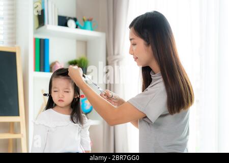 Asiatische Mutter Haare schneiden ihre Tochter im Wohnzimmer zu Hause während zu Hause bleiben sicher von Covid-19 Coronavirus während der Sperrung. Selbstquarantäne an Stockfoto