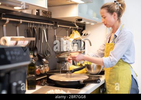 Übernachten Sie zu Hause Hausfrau Frau, die in der Küche kocht, rühren Sie Frittiergericht in einem Topf, und bereiten Sie Essen für das Familienessen zu. Stockfoto