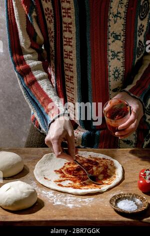 Frau in gestrickten Pullover Kochen italienische Pizza napolitana. Verteilen Sie frische hausgemachte Weizenteig mit Tomatensauce. Zutaten in Keramikplatten oben auf Stockfoto