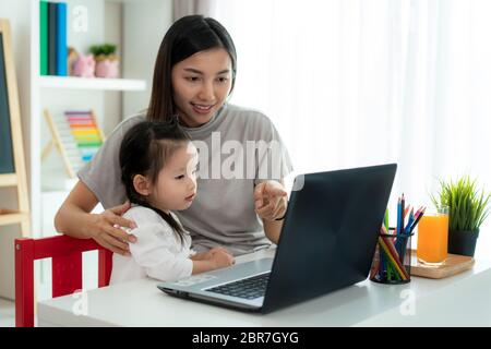 Asiatische Kindergarten Schule Mädchen mit Mutter Videokonferenz E-Learning mit Lehrer auf Laptop im Wohnzimmer zu Hause. Homeschooling und Abstand lear Stockfoto