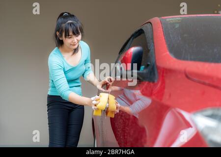 Asiatische Frau mit glücklich in Haus Waschbesitzer rotes Auto mit Seifenkämmen und Schwamm während des Aufenthalts zu Hause mit Freizeit über ihre tägliche Reinigung Stockfoto