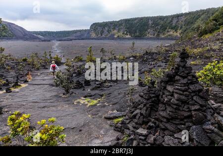 Menschen wandern auf dem Kraterboden des Kilauea Iki Krater und Pu'U PUA'i (Gushing Hill) mit dem dampfenden Kilauea Krater in der Ferne, April 2017 A Stockfoto