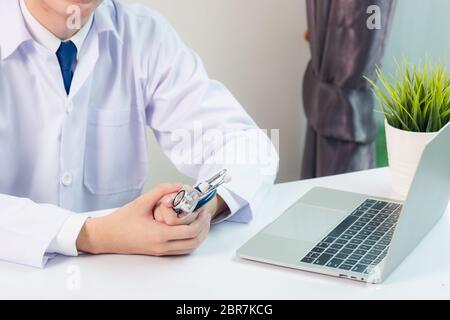 Mediziner arbeitet am Schreibtisch. Nahaufnahme des Stethoskops. Arzt Mann Videoanruf sitzen Hand in Hand und hören Patienten erklären auf der Vorderseite Laptop Comput Stockfoto