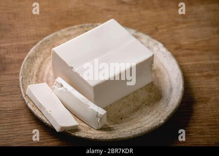 Seidentofu japanischer Sojakäse Vollstück auf Keramikplatte mit Essstäbchen über Holztisch. Stockfoto