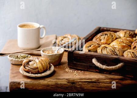 Traditionelle schwedische Kardamom süße Brötchen Kanelbulle in Holztablett, Tasse Kaffee, Zutaten in Keramikschale oben auf Holztisch. Stockfoto