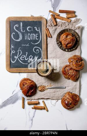 Traditionelle schwedische Zimt süßen Brötchen Kanelbulle auf Vintage-Tablett, Tasse Kaffee auf Leinentuch, Kreidetafel handgeschriebene Schriftzüge zu Hause bleiben und entspannen Stockfoto