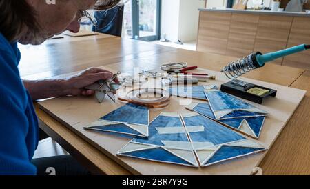 Frau arbeitet an Hobby Handwerk Buntglasscheiben für Lampenschirm mit Werkzeugen, Schottland, Großbritannien Stockfoto