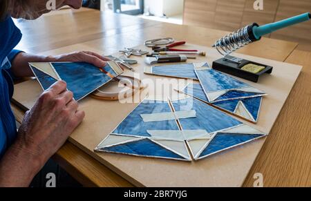 Frau arbeitet an Hobby Handwerk Buntglasscheiben für Lampenschirm mit Werkzeugen, Schottland, Großbritannien Stockfoto