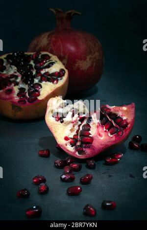 Granatapfel ganz und in Stücken mit verstreuten Samen auf dunklem Hintergrund. Stockfoto