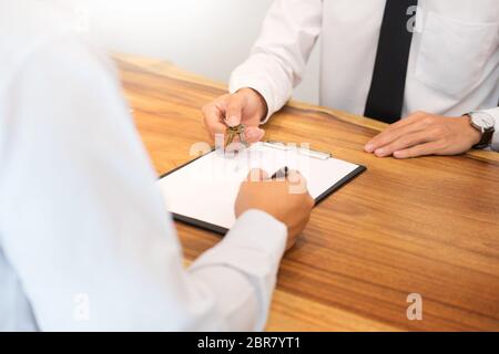 Immobilienmakler in Anzug sitzt in einem Büro Schreibtisch Übergabe der Hausschlüssel mit Kunden nach Vertragsunterzeichnung. Stockfoto