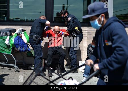 New York City, USA. Mai 2020. Zwei Beamte der NYPD helfen einem Mann (roter Pullover), sich hinzusetzen, nachdem er auf dem Bürgersteig am Broadway in Elmhurst, Queens, NY, am 20. Mai 2020 gefunden wurde. Dort, um Gesichtsmasken an eine Gruppe von Männern, die obdachlos erschienen, der Mann war nicht ansprechbar, als sie ankamen. (Anthony Behar/Sipa USA) Credit: SIPA USA/Alamy Live News Stockfoto