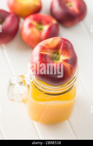 Flache Nektarinen und Saft Glas auf weißen Tisch Reif. Stockfoto