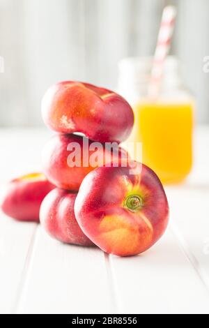 Flache Nektarinen und Saft Glas auf weißen Tisch Reif. Stockfoto