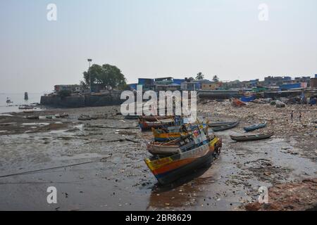 Fischerboote bei Ebbe neben einem stark verschmutzten Strand und Slum in Colaba, Mumbai, Indien. Stockfoto