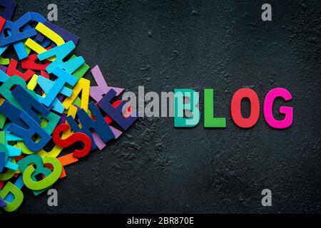 Die bunten Worten "BLOG" mit Holz Buchstaben neben einem Stapel der anderen Buchstaben auf dunklem Hintergrund. Stockfoto