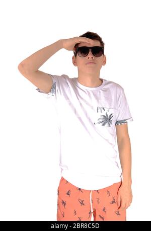 Ein hochgewachsener junger Teenager Jungen in einem weißem T-Shirt und Bermuda Shorts tragen Sonnenbrillen kost Weg suchen, auf weißem Hintergrund Stockfoto