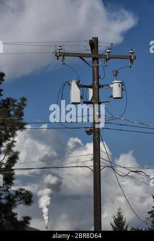 Ein Schornstein-Schornstein übersät dicken weißen Rauch aus einer Zellstoffmühle in einen trüben und blauen Himmel hinter den Drähten auf einem Telefon und Mast in Kamloops Stockfoto