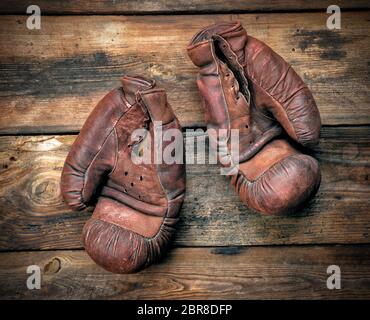 Sehr alte Leder braun Boxhandschuhe auf einem schäbigen Holzbrett Stockfoto