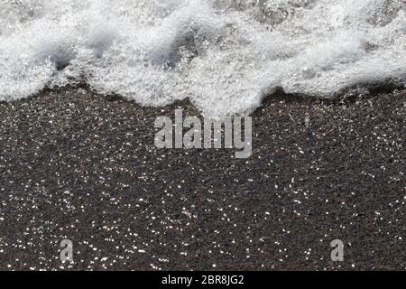 Wave Schaum auf dem Sand. Nahaufnahme des Meeres Wellen mit weißen Schaum auf dem sandigen Ufer mit Sun Reflexionen Wirkung. Stockfoto