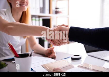 Lächelnd Geschäftsfrau zitternden Hand mit ihrer Kollegin über Schreibtisch am Arbeitsplatz Stockfoto