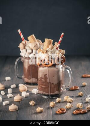 Nahaufnahme von zwei freakshake in Mason jar auf braunen Tisch. Ausgeflippt Milchshake mit Schokolade, Brezel, Eibisch, Popcorn und Waffeln. Trendy Essen Stockfoto