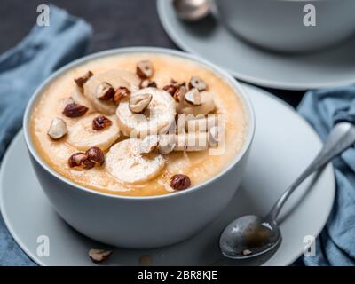 Zwei Schüssel mit Mais Grieß Brei mit Banane, Haselnuss und verbrannte Butter Honig. Süße Polenta oder maismehl Porridge auf schwarz Tischplatte. Ideen und recip Stockfoto