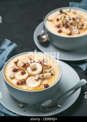 Zwei Schüssel mit Mais Grieß Brei mit Banane, Haselnuss und verbrannte Butter Honig. Süße Polenta oder maismehl Porridge auf schwarz Tischplatte. Ideen und recip Stockfoto