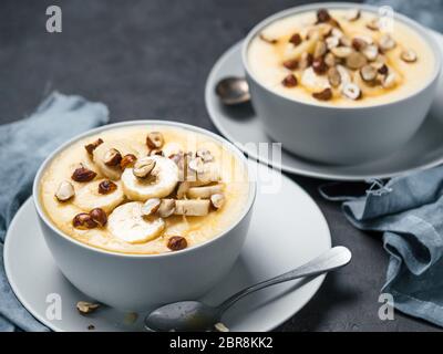 Zwei Schüssel mit Mais Grieß Brei mit Banane, Haselnuss und verbrannte Butter Honig. Süße Polenta oder maismehl Porridge auf schwarz Tischplatte. Ideen und recip Stockfoto