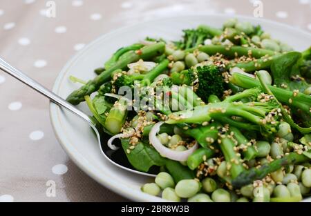 Mit Löffel in ein grünes Frühjahr Salat von Broccolini, Saubohnen, Schalotten und grüne Bohnen, bestreut mit nigella und Sesam Stockfoto