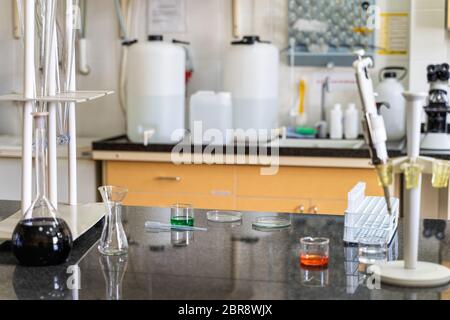 Pipette und bunten chemischen flüssigen Lösungen in Fässern an Labor Arbeitsplatte, Laborgeräte und Glaswaren im Hintergrund Stockfoto