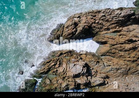 Luftaufnahme von Drohnen auf die wunderschönen Wellen des Ozeans, die an der felsigen Inselküste zusammenbrechen Stockfoto