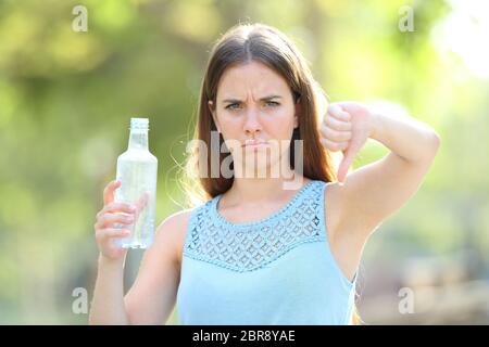 Wütende Frau Holding eine Plastikflasche mit thums in einem Park mit grünem Hintergrund Stockfoto