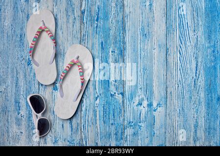 Strandaccessoires: Weiße weibliche Flip Flops und Sonnenbrille auf blauem Holzhintergrund. Draufsicht mit Kopierbereich. Konzept von Urlaub und Reisen am Meer. Summe Stockfoto