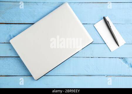 Grau Laptop und Notizbuch aus Papier mit schwarzer Tinte auf Blau Holz- Hintergrund. Der Blick von oben Stockfoto