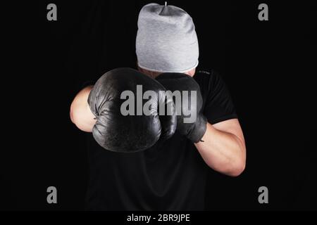 Junge Mann steht in einem Rack, das Tragen von sehr alten Vintage Brown Boxhandschuhe auf seinen Händen, schwarzer Hintergrund Stockfoto