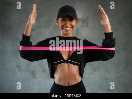 Glückliche gesunde lächelnde Frau, die mit Widerstandsband im Fitnessstudio arbeitet. Sportswoman führt Übungen für die Muskeln der Brust Stockfoto