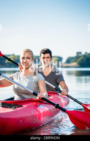 Lächelndes junges Paar mit Paddeln beim Kajakfahren auf dem See Stockfoto